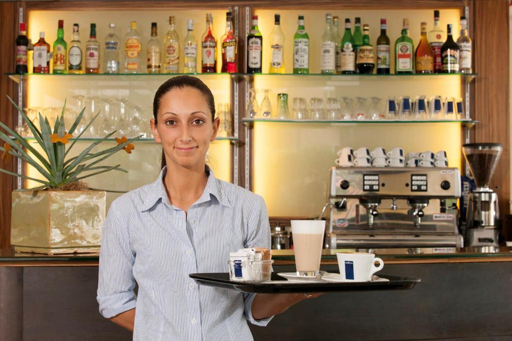 a woman holding a tray with a cup of coffee at Il Teatro in Lido di Jesolo