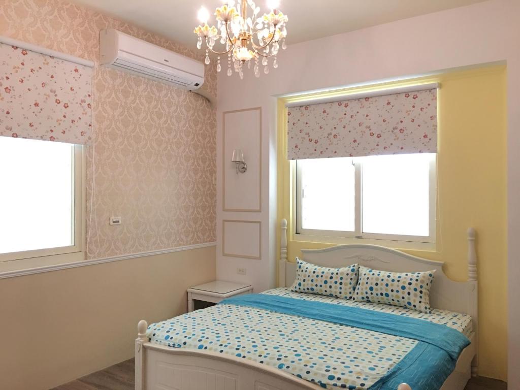 a bedroom with a bed and two windows and a chandelier at Ｗhite Ｗindmill in Hualien City