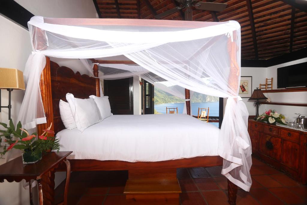 1 dormitorio con cama con dosel y sábanas blancas en Caille Blanc Villa & Hotel, en Soufrière