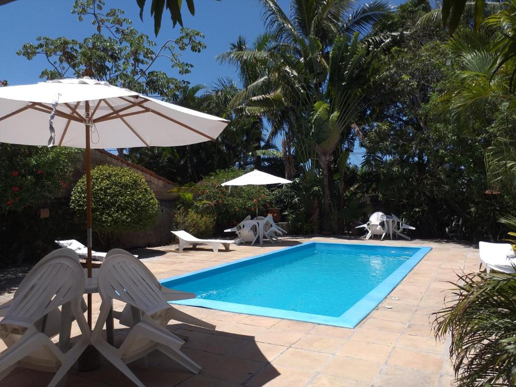 a swimming pool with two chairs and an umbrella at Residencial Coroa Vermelha in Santa Cruz Cabrália