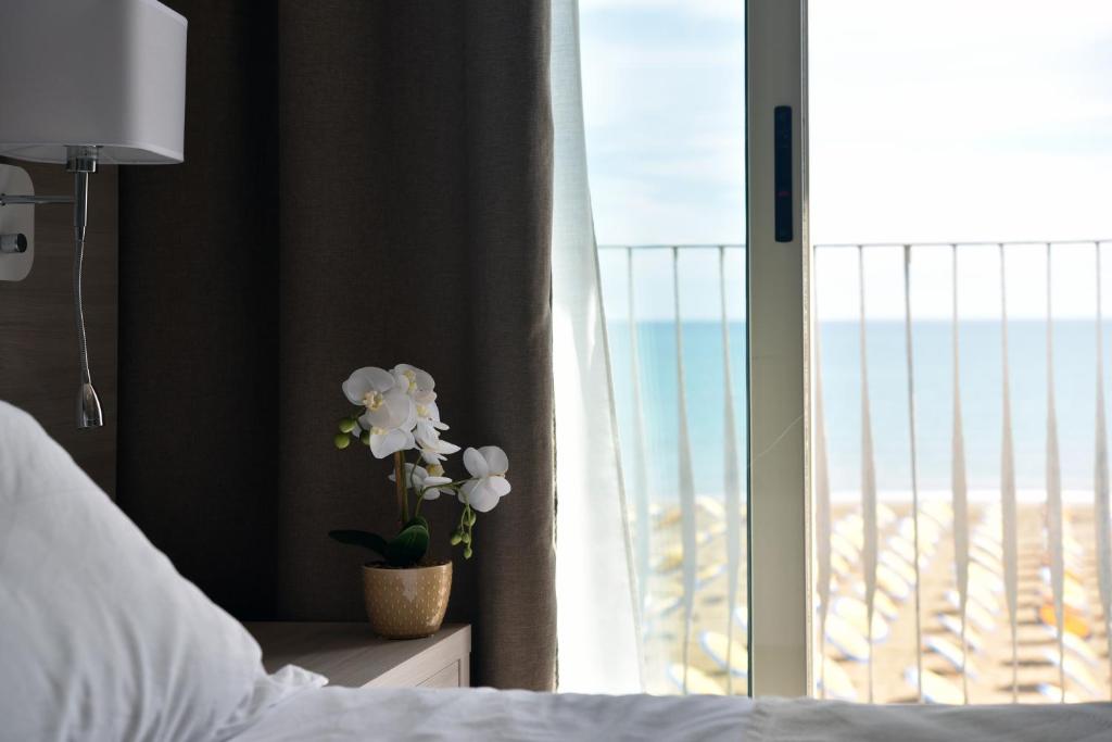 una camera da letto con finestra e vaso con fiori bianchi di Hotel Solemare - Frontemare - 3 Stelle Superior a Lido di Jesolo