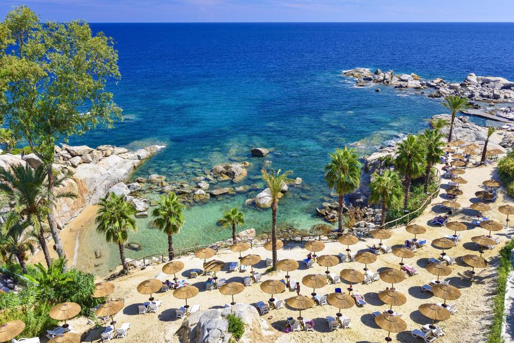 a beach with chairs and umbrellas and the ocean at Arbatax Park Resort - Cottage in Àrbatax