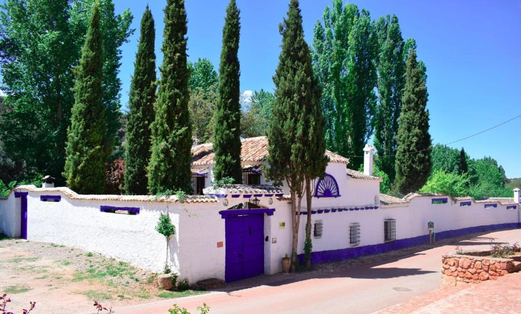 Casa blanca con puertas moradas y árboles en Venta del Celemín, en Ossa de Montiel