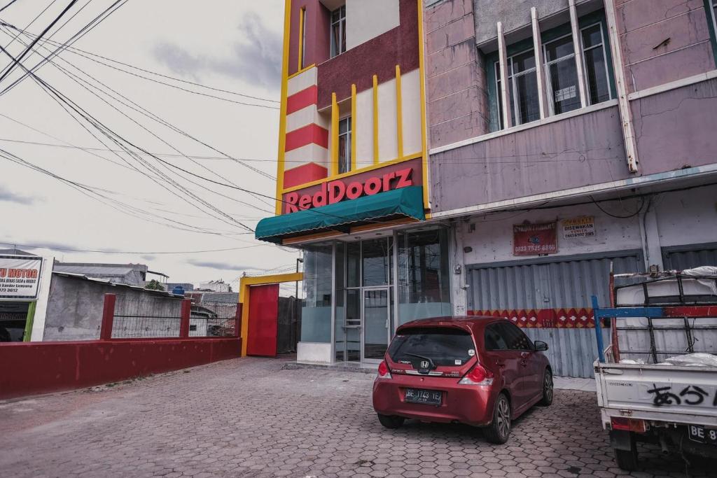 RedDoorz @ Jalan Pangeran Antasari Lampung 2 في Lampung: سيارة حمراء صغيرة متوقفة أمام مبنى