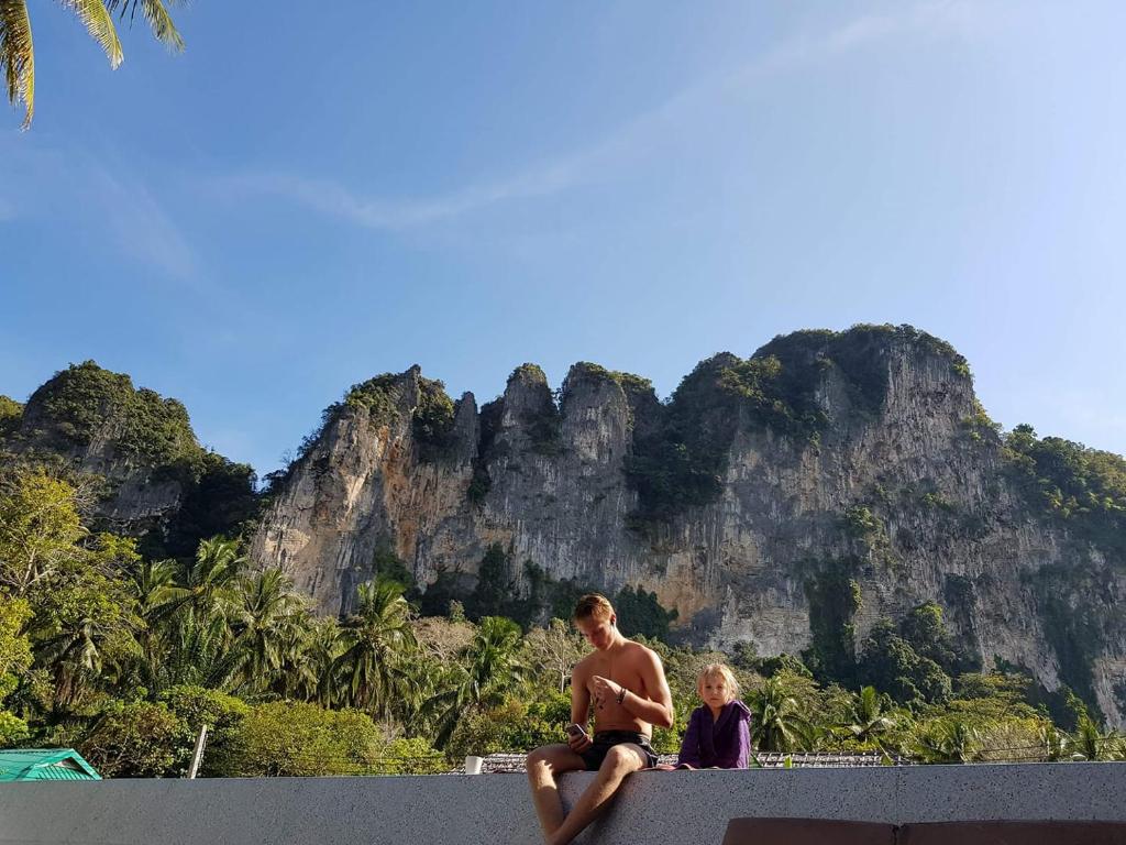 un hombre y un niño sentados en una pared con una montaña en Aonang Lodge - SHA, en Ao Nang Beach