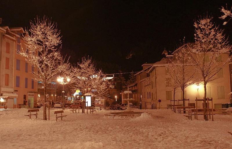 a snow covered street with benches and trees at night at Ax Vacances Famille in Ax-les-Thermes