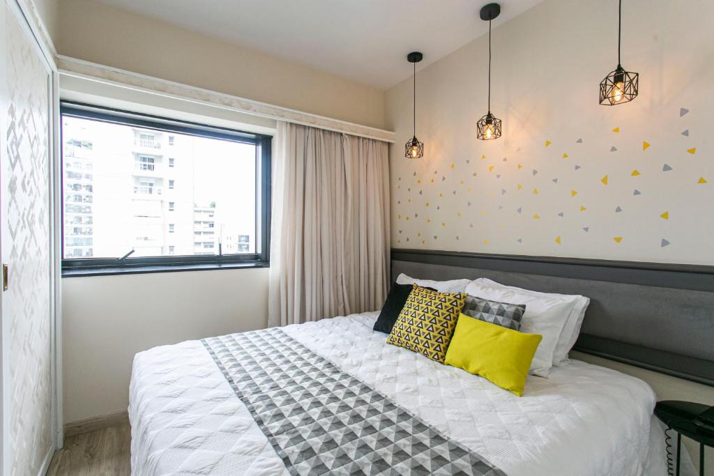 1 dormitorio con cama blanca y almohadas amarillas en Flat Privado Jardins, en São Paulo