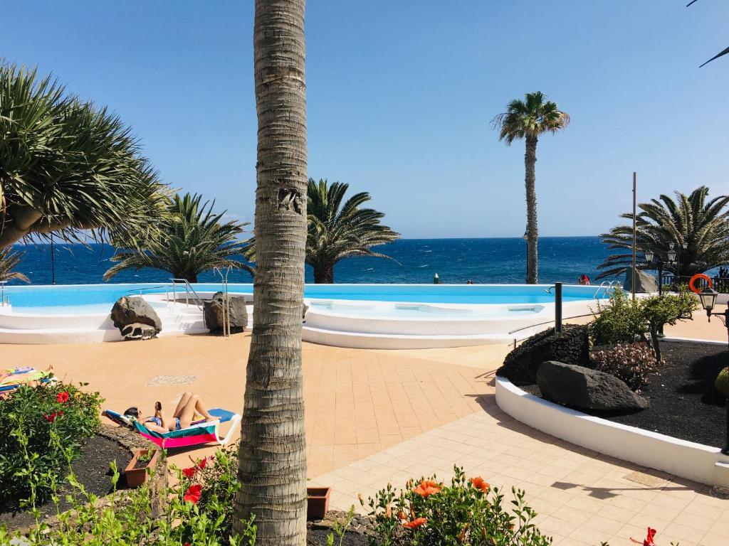 - une piscine avec des palmiers et des personnes sur la plage dans l'établissement EL Drago, à Costa Teguise