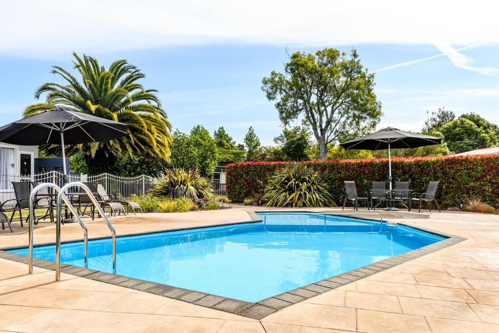 een zwembad met parasols, tafels en stoelen bij Motueka Garden Motel in Motueka