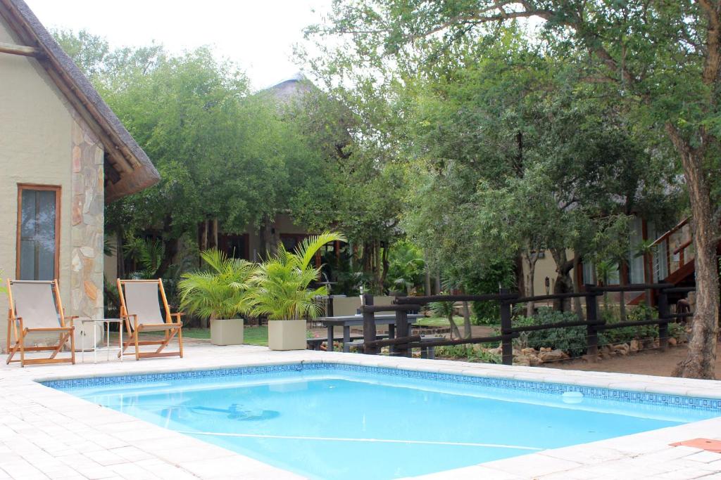 a swimming pool with two chairs next to a house at Woodpecker Lodge B&B in Hoedspruit