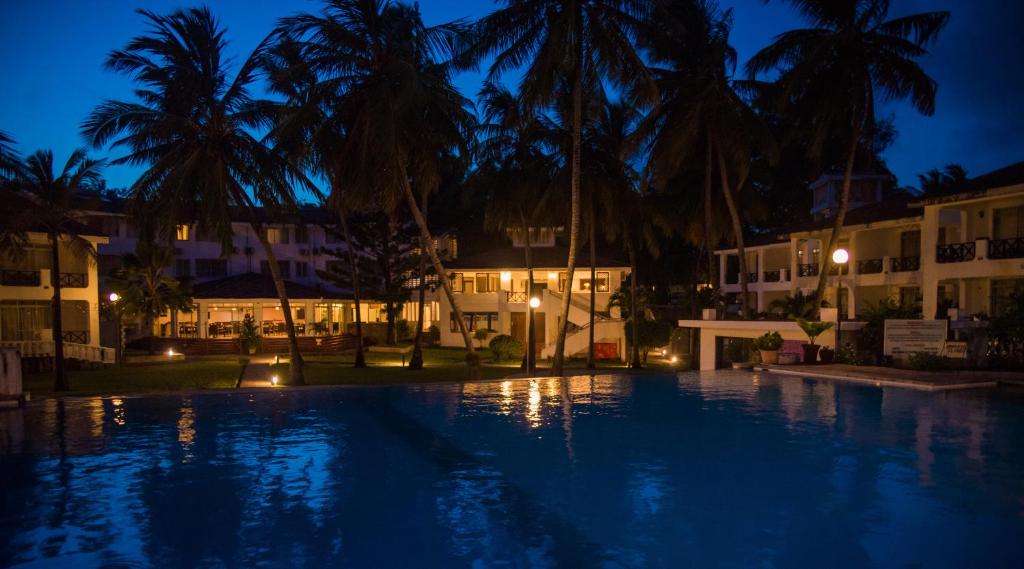 - une piscine de nuit avec des palmiers et des bâtiments dans l'établissement Nyali Beach Holiday Resort, à Nyali