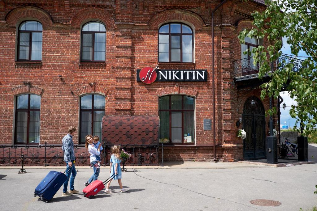una familia con equipaje caminando frente a un edificio en Nikitin Hotel, en Nizhny Novgorod