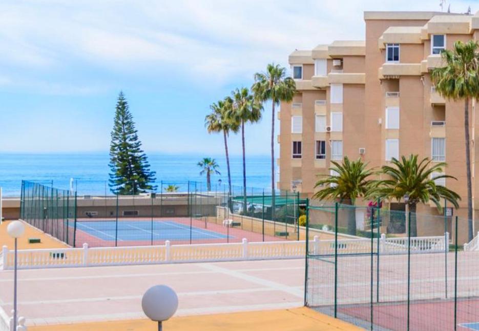 einen Tennisplatz mit Palmen und ein Gebäude in der Unterkunft Apartamento costa del oro in Torrox Costa