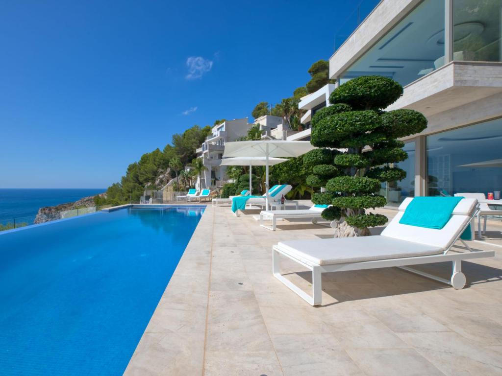 a pool with lounge chairs and a tree next to a building at Villa Emma on the Roc by Interhome in Jávea