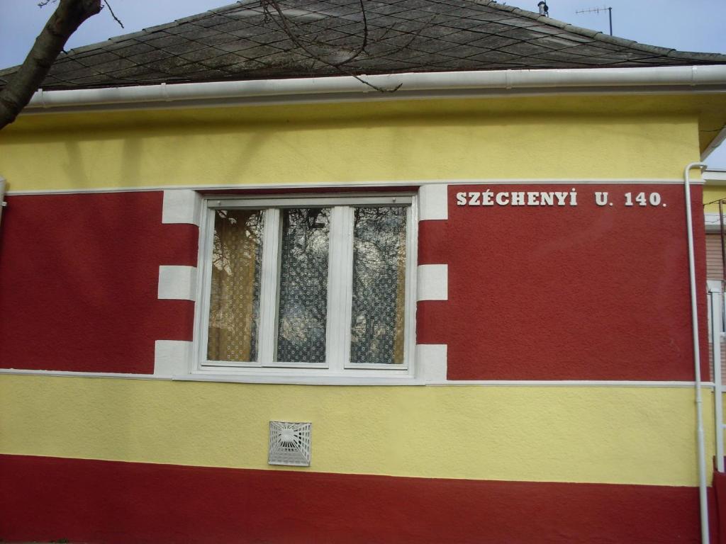 a red yellow and red house with a window at Kereki Retro Vendégház in Kerekegyháza