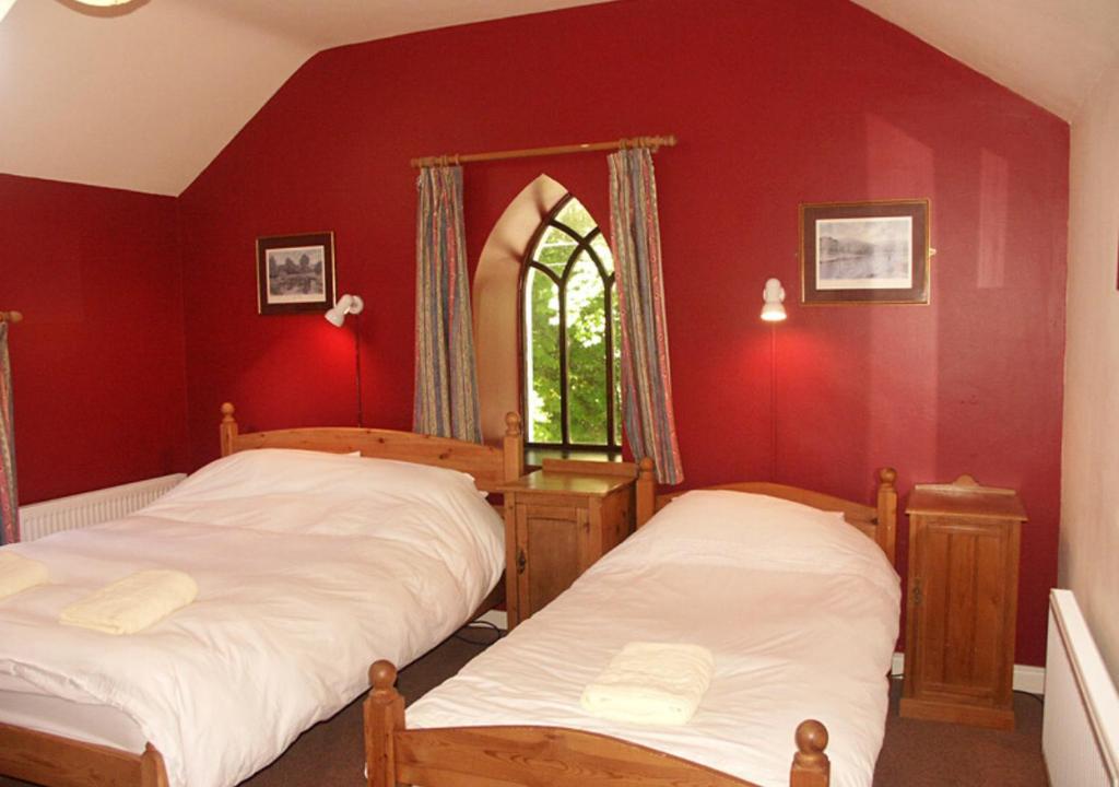 two beds in a room with red walls and a window at Delphi Lodge in Leenaun