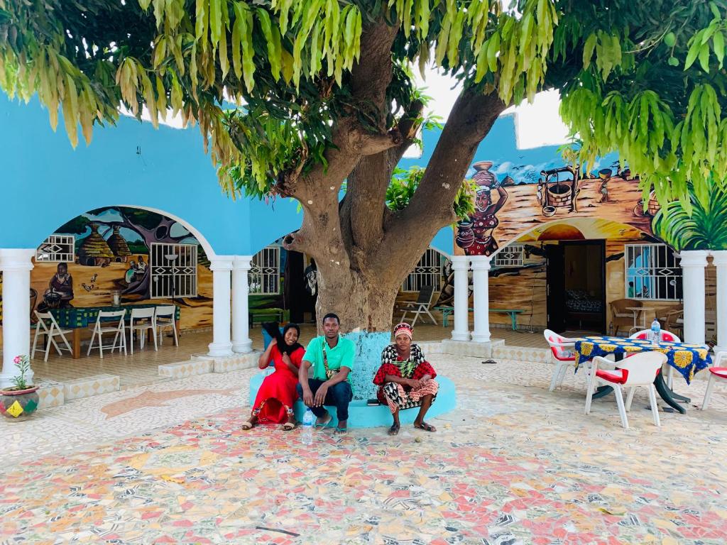 eine Gruppe von Menschen, die auf einer blauen Couch unter einem Baum sitzen in der Unterkunft Bajo Kunda - Guesthouse in Kololi