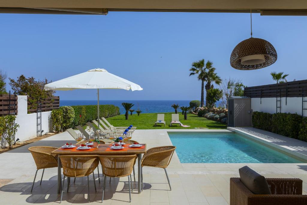 mesa de comedor con sillas y sombrilla junto a la piscina en Protaras Beachfront Villa Pietra, en Protaras