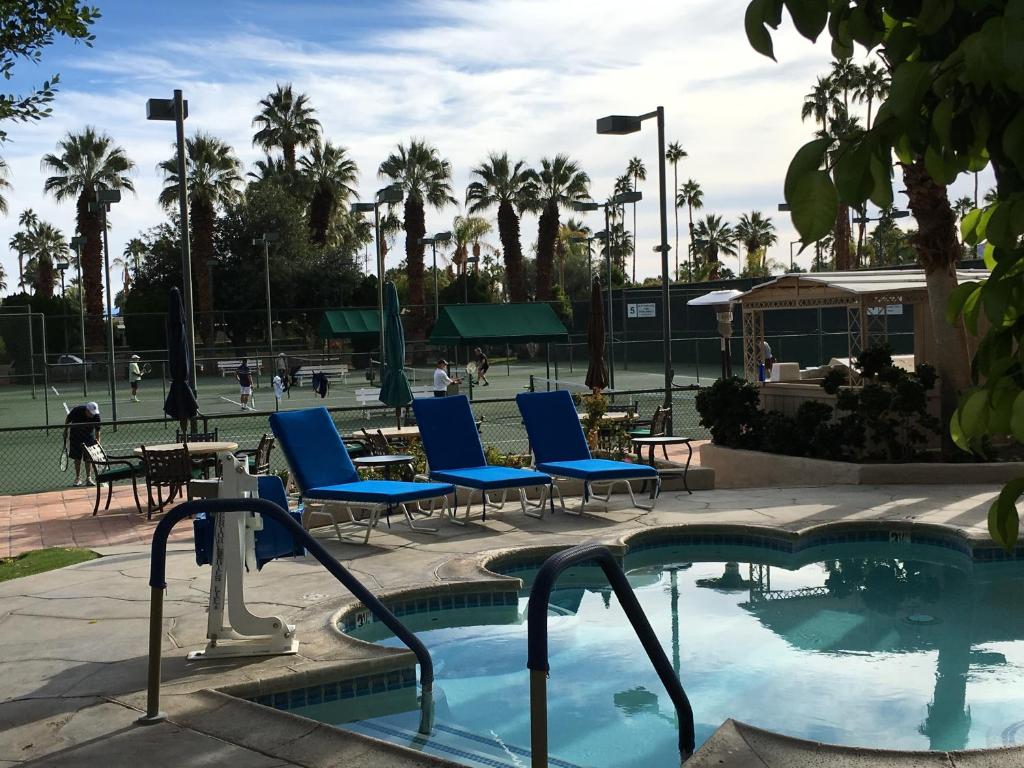 a swimming pool with blue chairs and a tennis court at GetAways at Palm Springs Tennis Club in Palm Springs