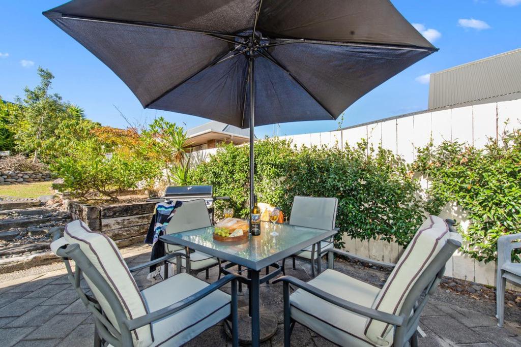a table and chairs with an umbrella on a patio at Sandcastles on Tay - Mt Maunganui Holiday Home in Mount Maunganui