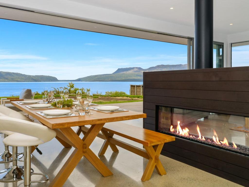 a dining room with a fireplace and a table and chairs at Mana Sarovar - Lake Tarawera Home in Lake Tarawera