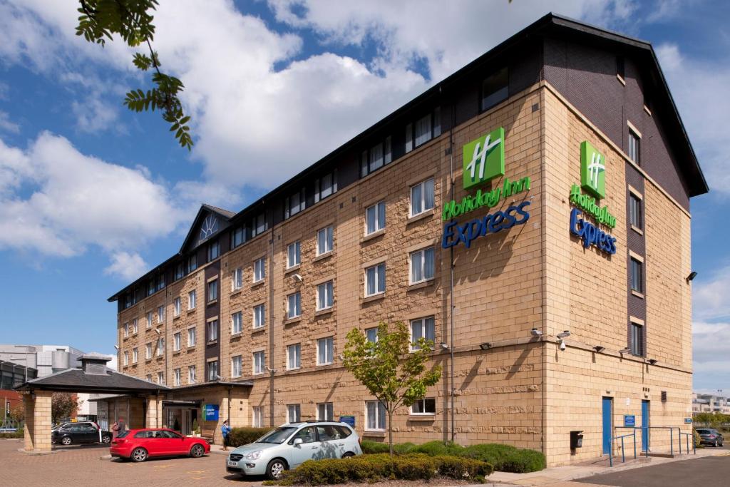 um grande edifício de tijolos com carros estacionados num parque de estacionamento em Holiday Inn Express Edinburgh - Leith Waterfront, an IHG Hotel em Edimburgo