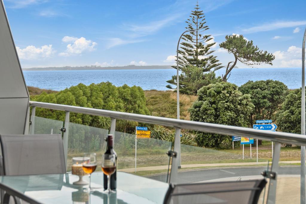 a table with two glasses of wine on a balcony at Sunrise, Seaviews and BBQs-Papamoa Beach Apartment in Papamoa