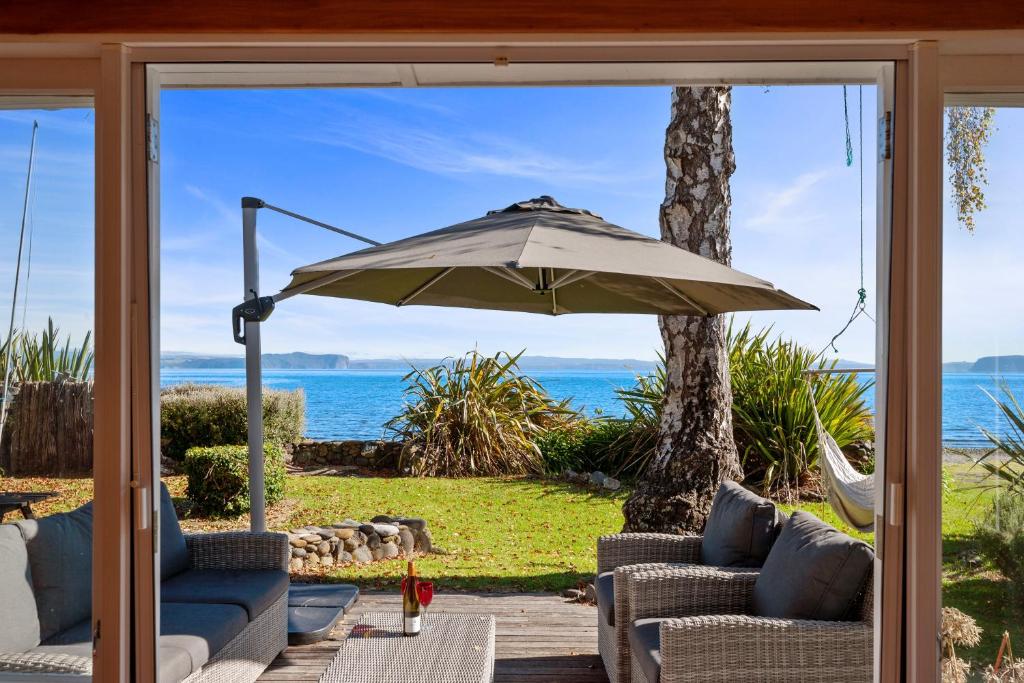 a patio with two chairs and an umbrella at North Cole Cottage - Hatepe Lake Front Home in Waitahanui