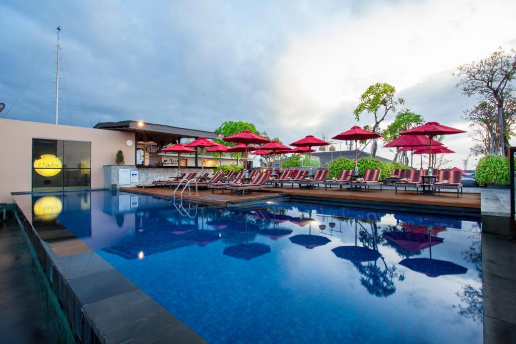 a swimming pool with red umbrellas and chairs at Sevn Legian in Legian