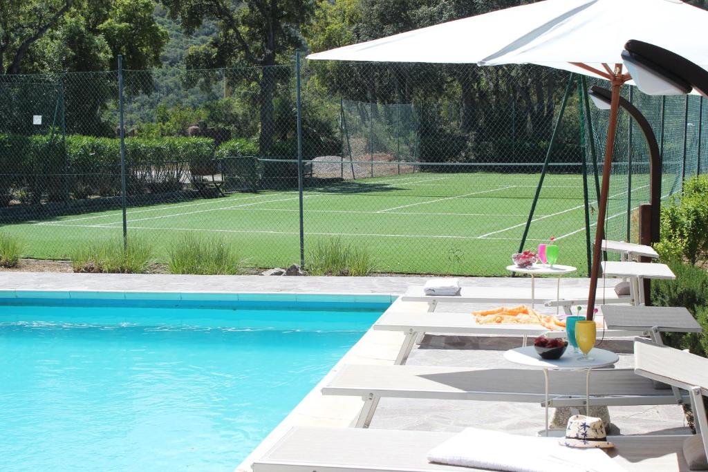 a pool with chairs and an umbrella and a tennis court at Villa EnriMar in Capoliveri