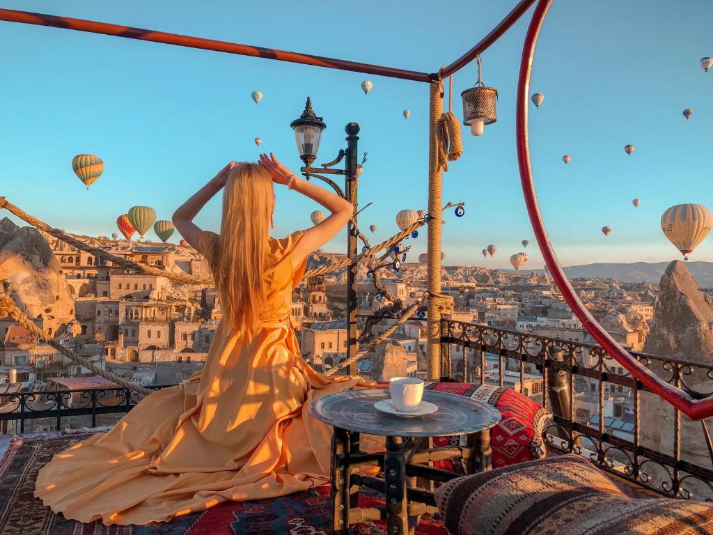 une femme debout sur un balcon avec montgolfières dans l'établissement Maccan Cave Hotel, à Gorëme