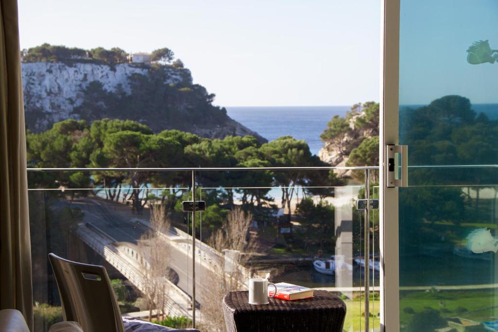 a room with a view of the ocean from a balcony at Minura Cala Galdana & Apartamentos d'Aljandar in Cala Galdana