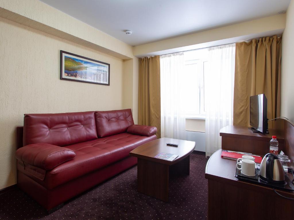 a living room with a red leather couch in a hotel room at AZIMUT Hotel Kemerovo in Kemerovo
