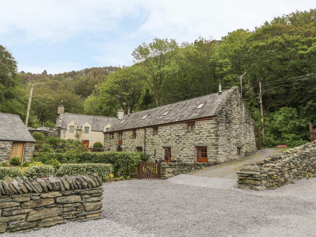 an old stone house with a stone wall and a fence at Hendoll Cottage 2 in Fairbourne