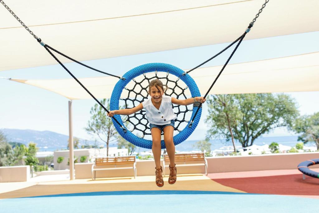 a girl is sitting on a swing at a playground at Ikos Dassia in Dassia