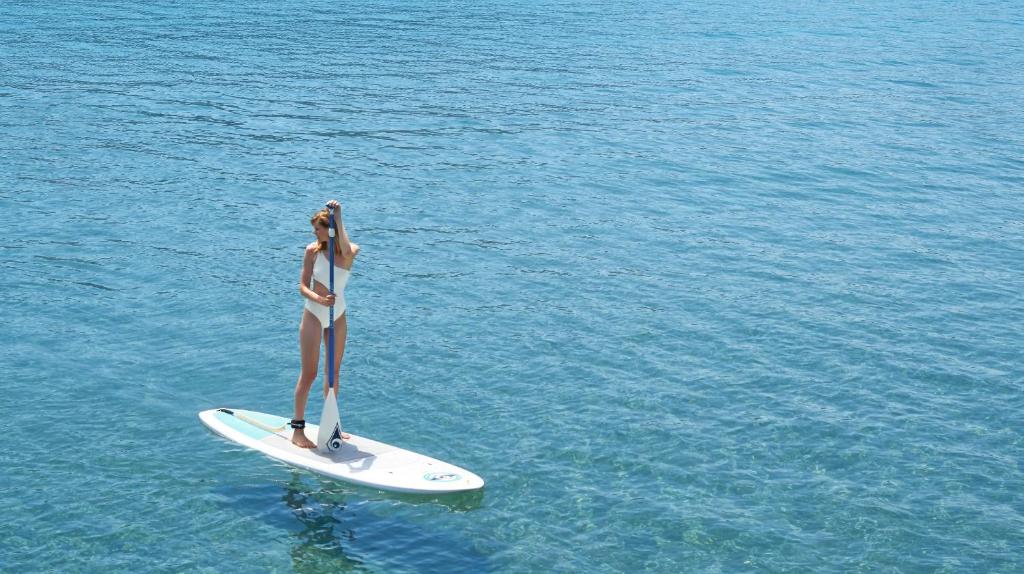 a woman is standing on a surfboard in the water at Ikos Dassia in Dassia