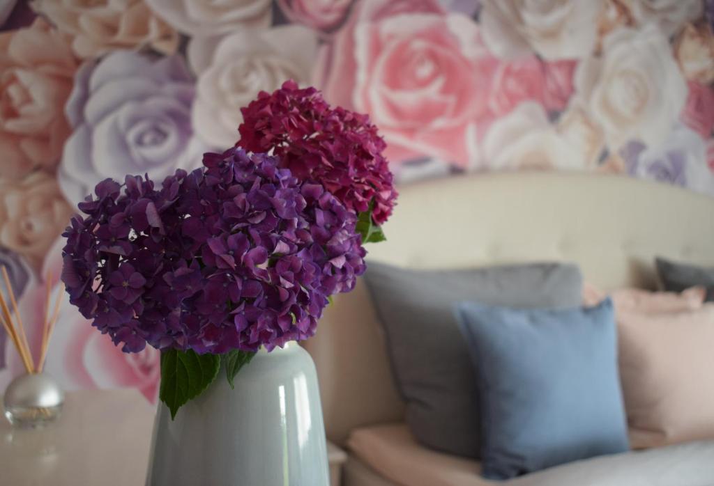 un vase blanc rempli de fleurs violettes à côté d'un canapé dans l'établissement Apartment Rose Sasbachwalden, à Sasbachwalden