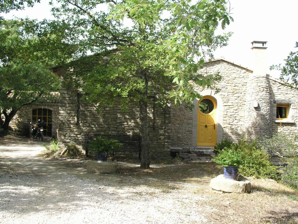 a brick building with a yellow door and a tree at La maison jaune in La Roque-sur-Pernes