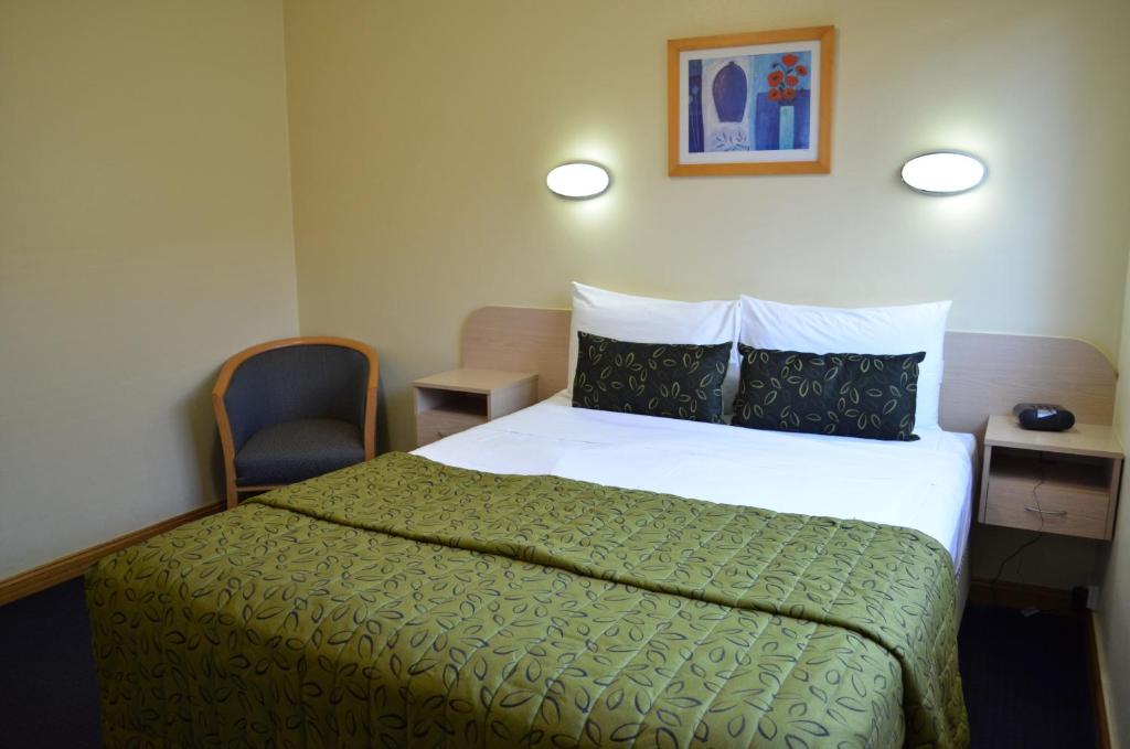 a bedroom with a bed with a green blanket and a chair at Airport Motel Brisbane in Brisbane