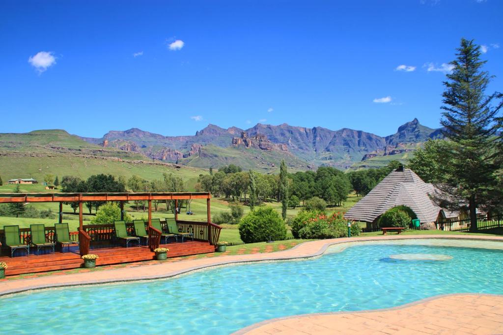 a swimming pool with chairs and a gazebo and mountains at Gooderson Leisure Fairways Self Catering and Timeshare Gold Crown Resort in Drakensberg Garden
