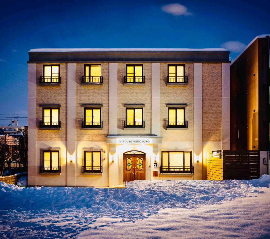 um grande edifício com as suas luzes acesas na neve em Miidokoro House Hotel em Sapporo