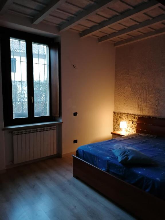 a bedroom with a bed with a blue comforter and two windows at Appartamento in storica Cascina Lombarda Cusago Rho-Fiera-San-Siro in Cusago