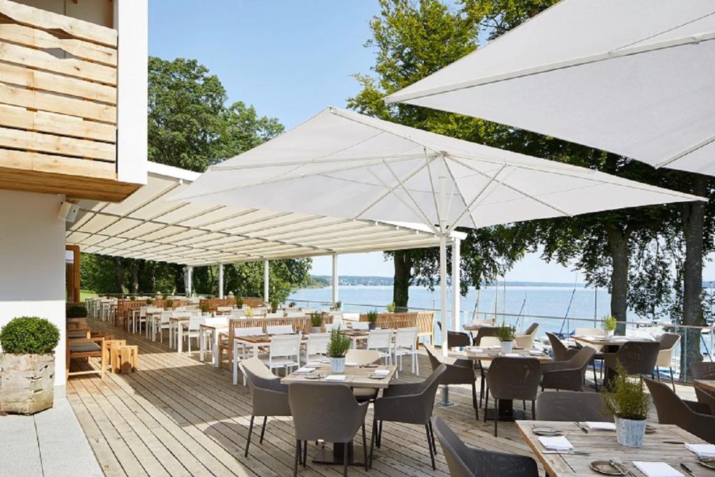 a restaurant with tables and white umbrellas on a deck at Marina Hotel am Starnberger See in Bernried