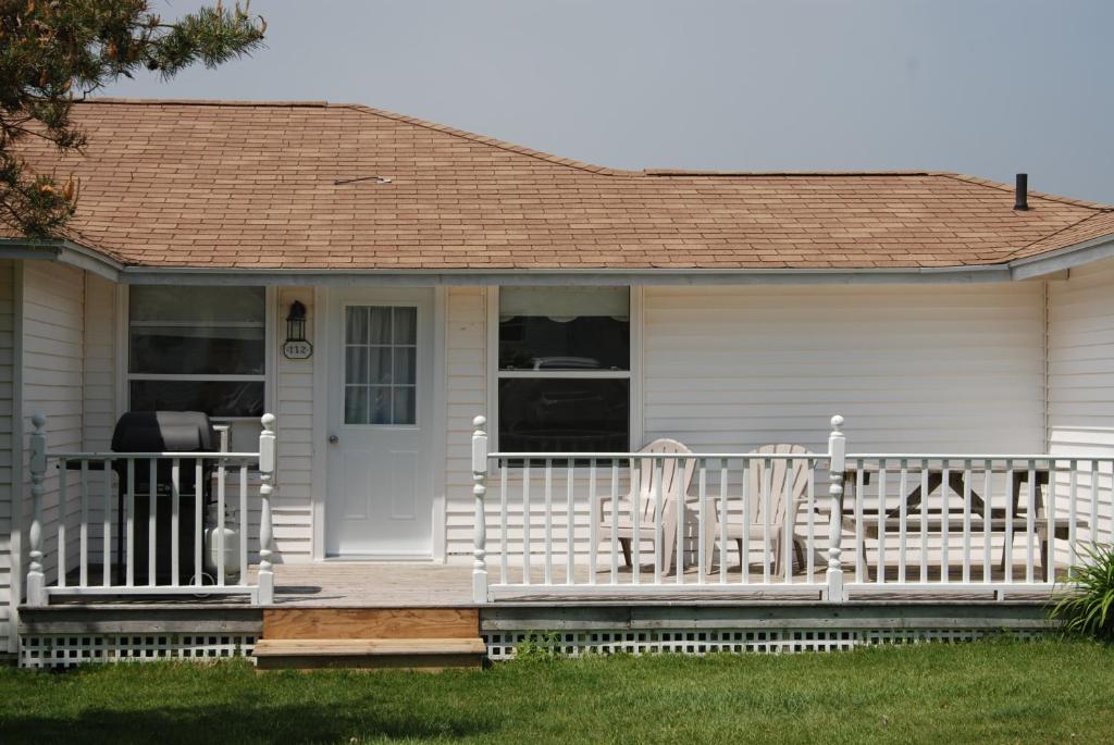 a white house with two chairs on a porch at Shining Waters - Ingleside Cottages in Cavendish