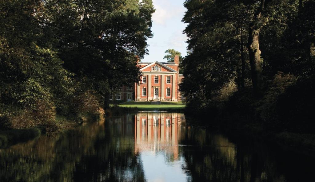 a large red house on the water with trees at Warbrook House Heritage Hotel in Hook