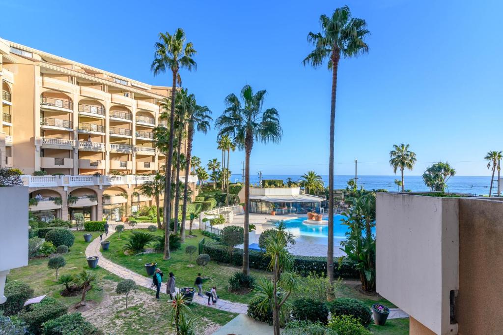 - une vue sur le complexe avec des palmiers et une piscine dans l'établissement LE PALM AZUR - vue mer sur les iles de Lérins, à Cannes