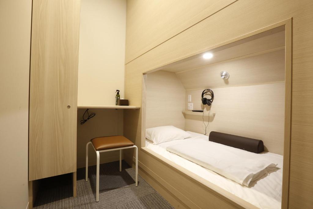 Grand Cabin Tenjin Minami في فوكوكا: غرفة نوم صغيرة بها سرير وكرسي