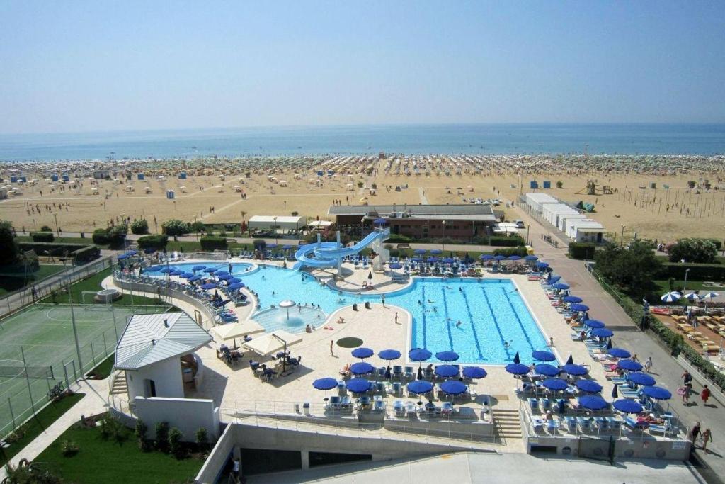 una piscina con sombrillas azules y una playa en Hotel Lido Bibione Beach, en Bibione