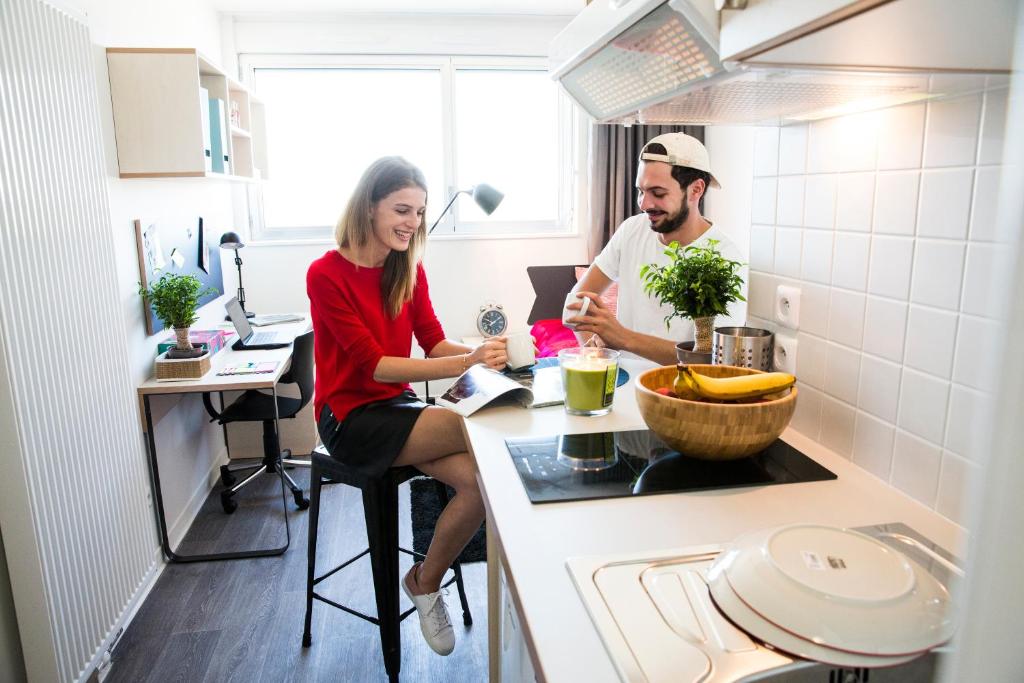 Un uomo e una donna seduti al bancone di una cucina di Résidence Kley Toulouse a Tolosa