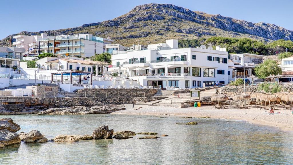 um grupo de edifícios numa praia ao lado de uma massa de água em Hoposa Niu em Cala de Sant Vicent